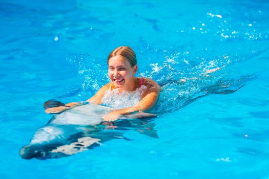 Happy little girl swimming with dolphins in Dolphinarium. Swimming, bathing and communication with dolphins.