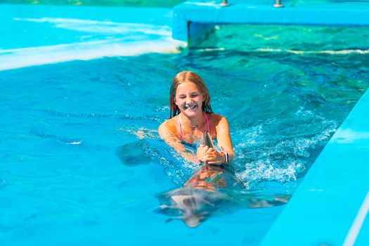 Happy little girl swimming with dolphins in Dolphinarium. Swimming, bathing and communication with dolphins.