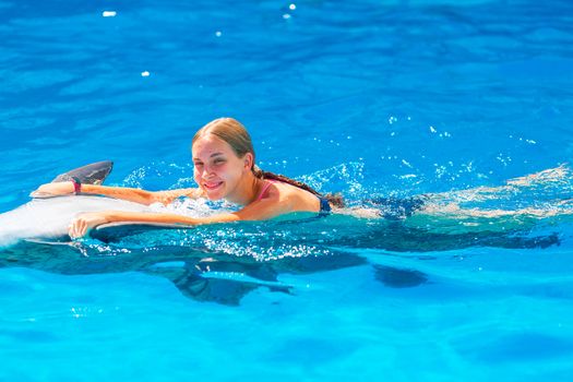 Happy little girl swimming with dolphins in Dolphinarium. Swimming, bathing and communication with dolphins.