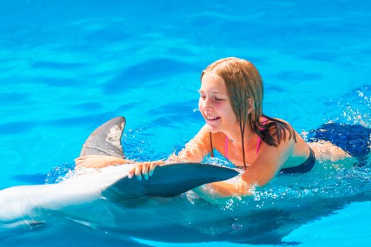 Happy little girl swimming with dolphins in Dolphinarium. Swimming, bathing and communication with dolphins.