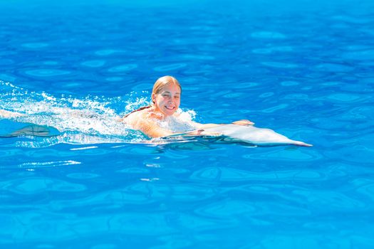 Happy little girl swimming with dolphins in Dolphinarium. Swimming, bathing and communication with dolphins.