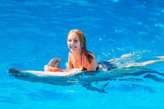 Happy little girl swimming with dolphins in Dolphinarium. Swimming, bathing and communication with dolphins.