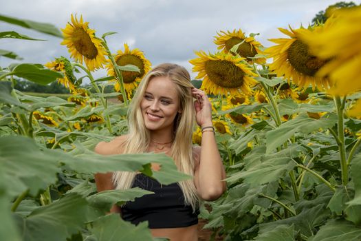 A gorgeous blonde model poses outdoors in a field of sunflowers while enjoying a summers day