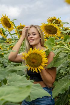 A gorgeous blonde model poses outdoors in a field of sunflowers while enjoying a summers day
