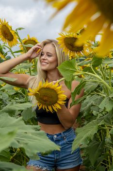A gorgeous blonde model poses outdoors in a field of sunflowers while enjoying a summers day