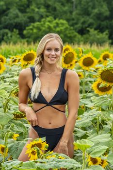 A gorgeous blonde model poses outdoors in a field of sunflowers while enjoying a summers day