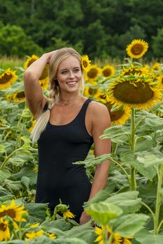 A gorgeous blonde model poses outdoors in a field of sunflowers while enjoying a summers day
