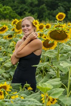 A gorgeous blonde model poses outdoors in a field of sunflowers while enjoying a summers day