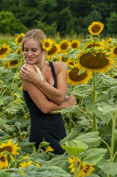 A gorgeous blonde model poses outdoors in a field of sunflowers while enjoying a summers day