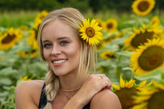 A gorgeous blonde model poses outdoors in a field of sunflowers while enjoying a summers day