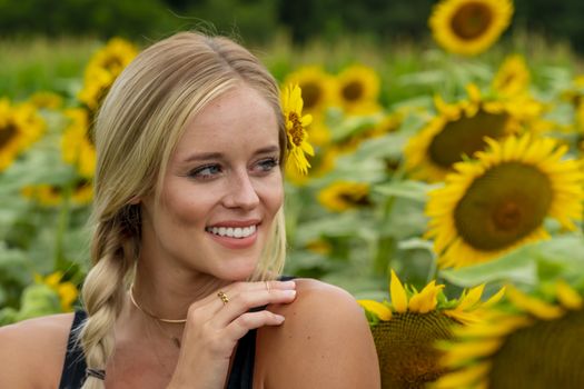 A gorgeous blonde model poses outdoors in a field of sunflowers while enjoying a summers day