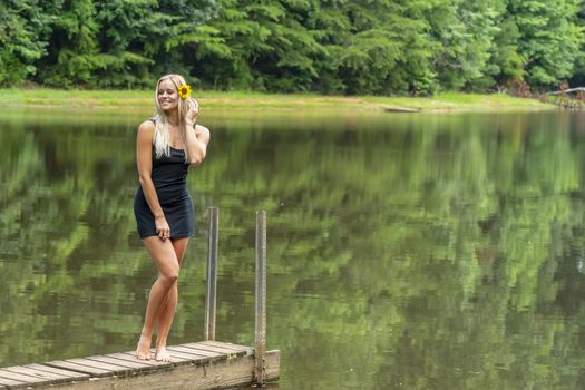 A gorgeous blonde model poses outdoors near a pond while enjoying a summers day