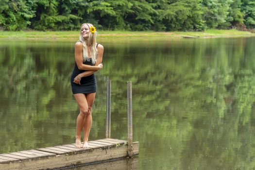 A gorgeous blonde model poses outdoors near a pond while enjoying a summers day