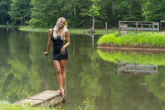 A gorgeous blonde model poses outdoors near a pond while enjoying a summers day