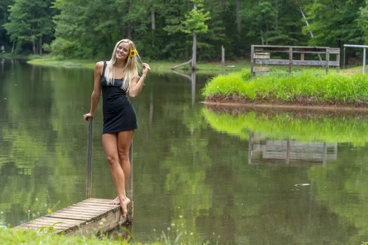 A gorgeous blonde model poses outdoors near a pond while enjoying a summers day