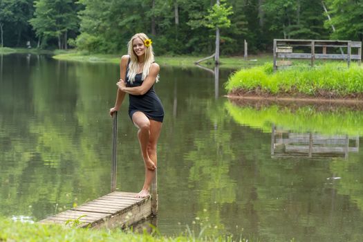 A gorgeous blonde model poses outdoors near a pond while enjoying a summers day