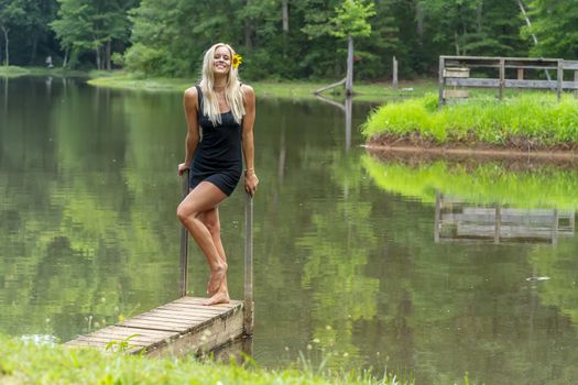 A gorgeous blonde model poses outdoors near a pond while enjoying a summers day