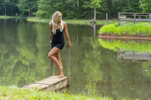 A gorgeous blonde model poses outdoors near a pond while enjoying a summers day