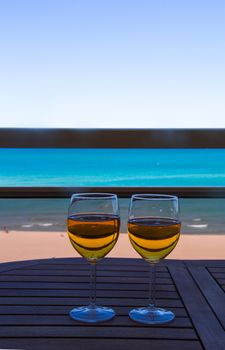 two glasses full of cider on top of a table with the sea in the background