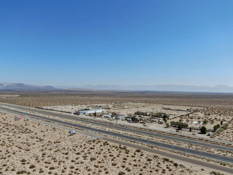 Aerial view of road in the middle of the desert under blue sky in California's Mojave desert, near Ridgecrest. Desert brush with road.