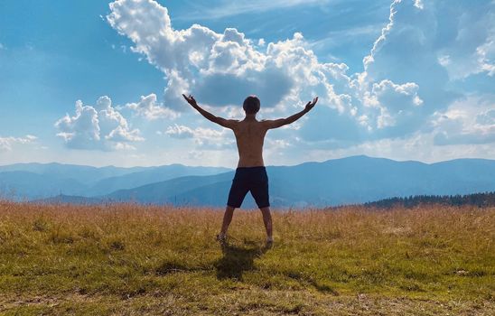 happy young man with arms raised	 among mountains