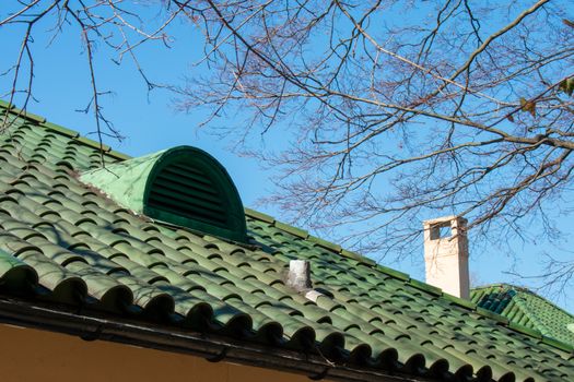 A Green Tile Roof on a Clear Blue Sky With a Vent in the Middle