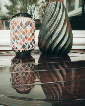 Two Detailed Vases on a Wet Brown Table Casting a Reflection on It