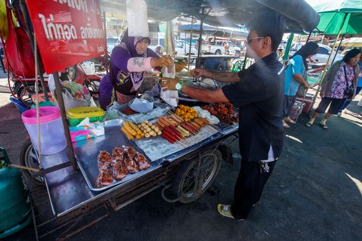 Khao Lak, Thailand - February 22, 2016:  Unknown man buying breakfast from local merchant with her mobile stall on morning market. Thai cuisine is renowned for its tasty food.