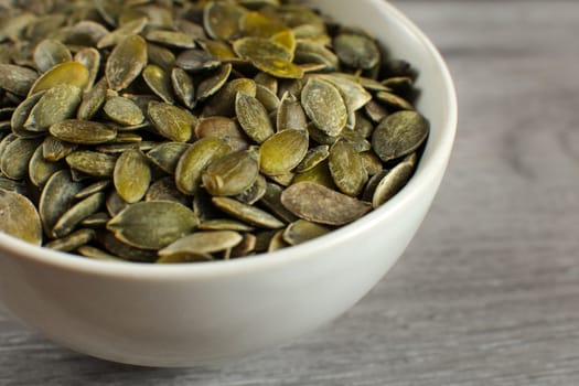 Detail on roasted salted pumpkin seeds placed in small ceramic bowl.