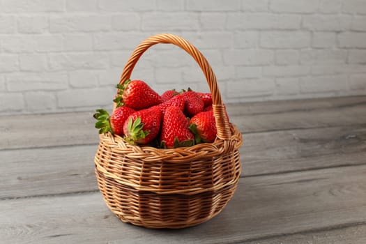 Small wicker basket full of strawberries placed on gray wood desk.