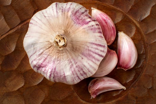 Close up view from above to garlic bulb and purple garlic cloves on carved wooden tray.