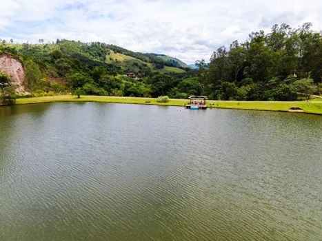 Aerial view of little wood cabana next the lake in the valley, with family enjoying relax moment, swimming and fishing. Monte Alegre Do Sul, Brazil. 