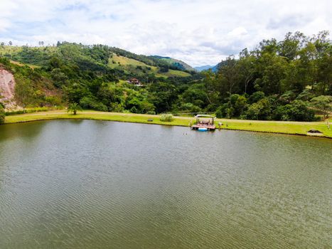 Aerial view of little wood cabana next the lake in the valley, with family enjoying relax moment, swimming and fishing. Monte Alegre Do Sul, Brazil. 