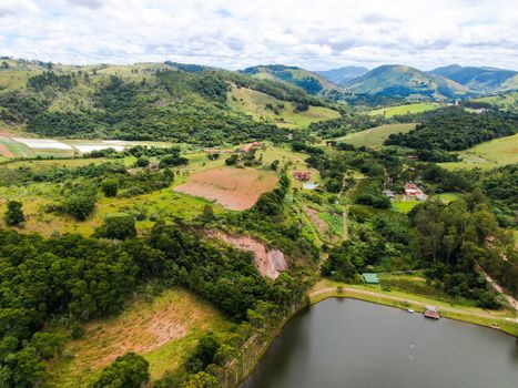 Aerial view of valley with lake, forest and villas in tropical country. Green mountain with forest on Brazil