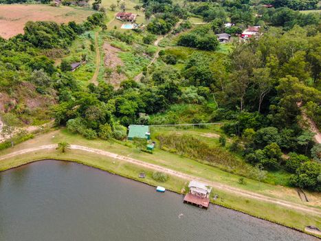 Aerial view of little wood cabana next the lake in the valley, with family enjoying relax moment, swimming and fishing. Monte Alegre Do Sul, Brazil. 