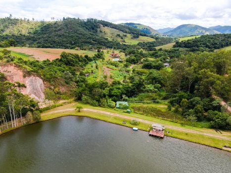 Aerial view of little wood cabana next the lake in the valley, with family enjoying relax moment, swimming and fishing. Monte Alegre Do Sul, Brazil. 