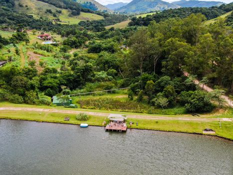 Aerial view of little wood cabana next the lake in the valley, with family enjoying relax moment, swimming and fishing. Monte Alegre Do Sul, Brazil. 