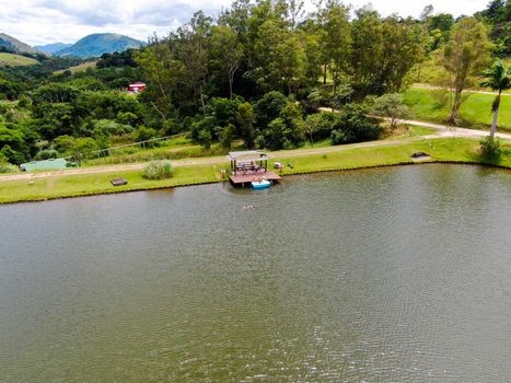Aerial view of little wood cabana next the lake in the valley, with family enjoying relax moment, swimming and fishing. Monte Alegre Do Sul, Brazil. 