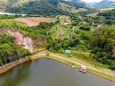 Aerial view of little wood cabana next the lake in the valley, with family enjoying relax moment, swimming and fishing. Monte Alegre Do Sul, Brazil. 