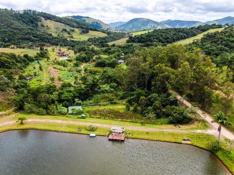 Aerial view of little wood cabana next the lake in the valley, with family enjoying relax moment, swimming and fishing. Monte Alegre Do Sul, Brazil. 