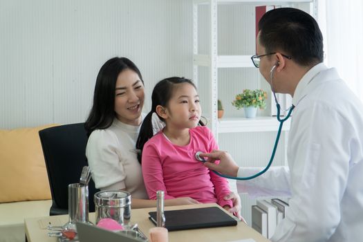 Asian adult mother and child daughter consulted a doctor at the clinic. Pediatricians perform medical checks on kid patients by using a stethoscope to listen to the heart.