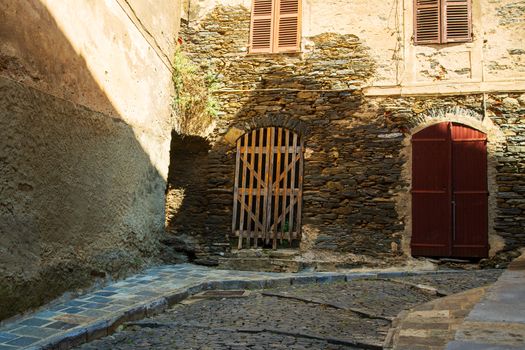 narrow alley with cobblestones in  a village on the isle of Corsica in France during summertime with a nice sunlight on the walls. The entrance of the houses are old wooden ports