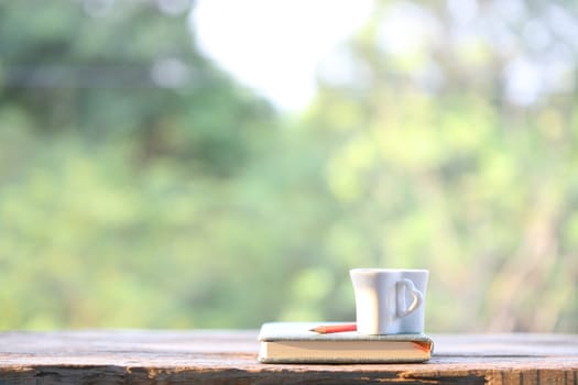 White cup with notebook on wooden table with nature view
