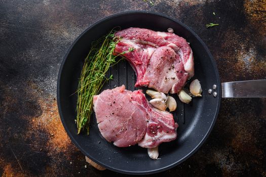 Juicy grilled pork steak with herbs on bone in grill frying pan hot with smoke and hot oil just from fire, top view cooking bone with seasonings rustic metal background.