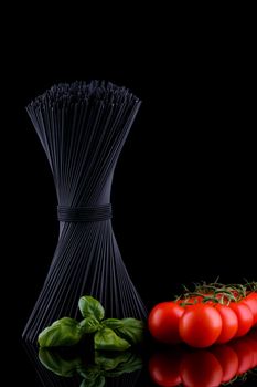 Black spaghetti with basel leaves and red tomato on black background.