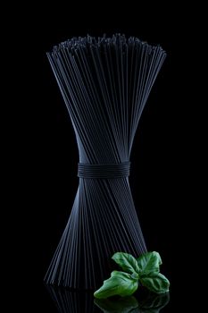 Black spaghetti with fresh green basel leaves with reflection on black background and place for text.