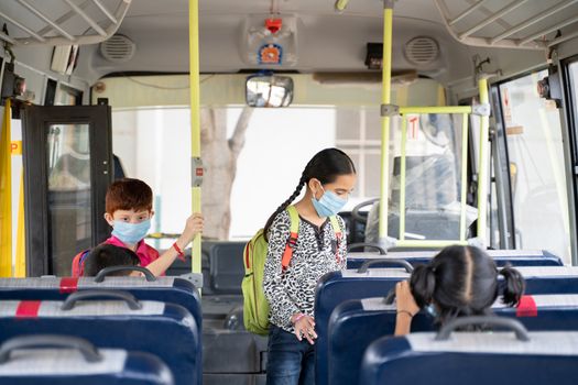 Kids with medical mask coming inside school bus and sitting on seats while maintaining social distance due to coronavirus or covid-19 pandemic - Concept of school reopen or back to school.