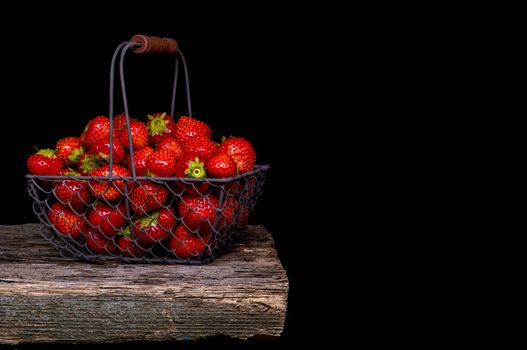 Strawberry with strawberry leaf in a metal basket on black background.