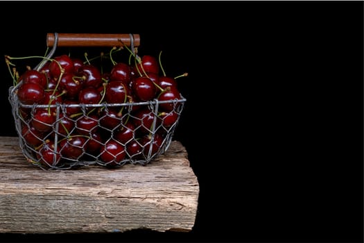 Fresh cherry fruit in a metal basket on black background.