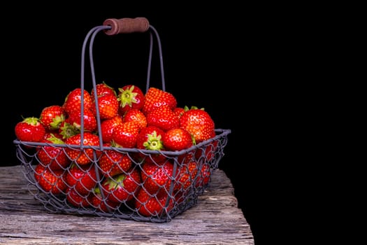 Strawberry with strawberry leaf in a metal basket on black background.